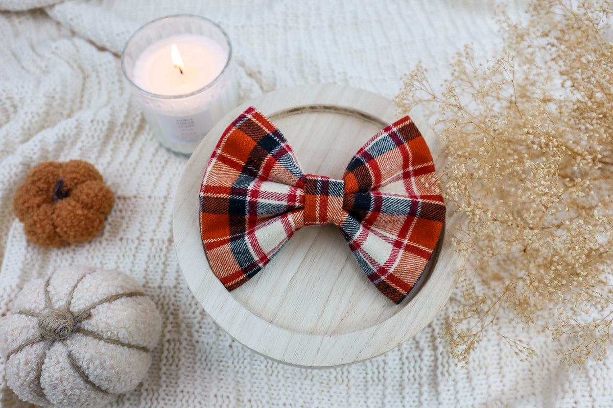 Plaid bow tie on a wooden plate with pumpkins and a candle in the background