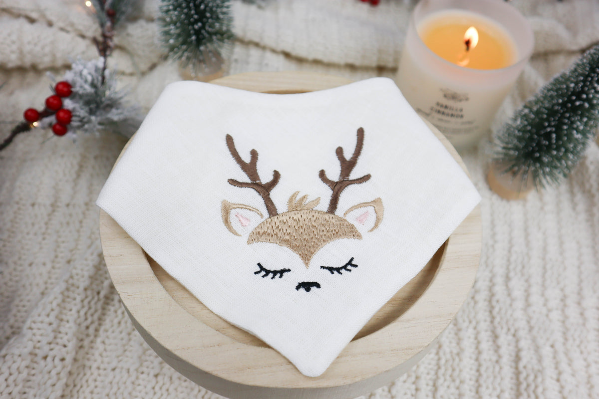 Embroidered dog bandana with deer design on a wooden plate, surrounded by festive decorations.