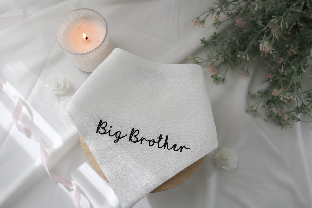 White bandana with 'Big Brother' text on a white surface with a candle and flowers.