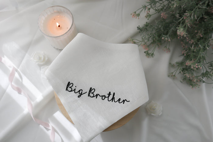 White bandana with 'Big Brother' text on a white surface with a candle and flowers.