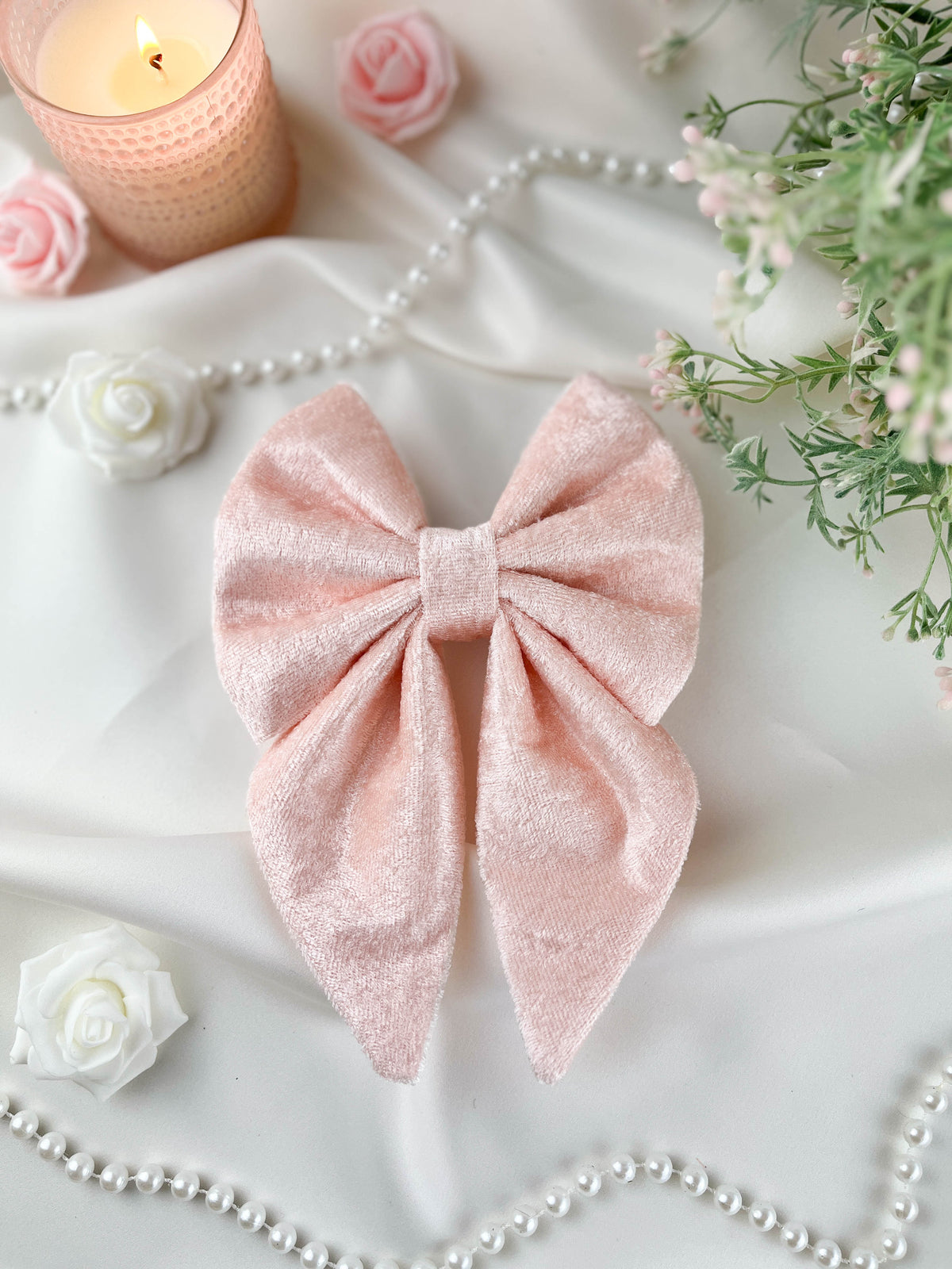 Pink bow with floral and candle decorations on a white surface