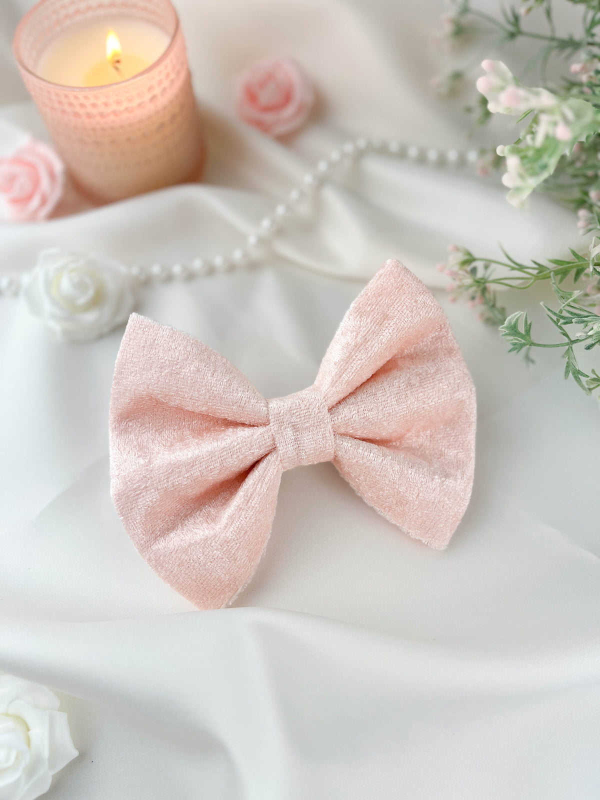 Pink bow tie on a white surface with flowers and a candle in the background