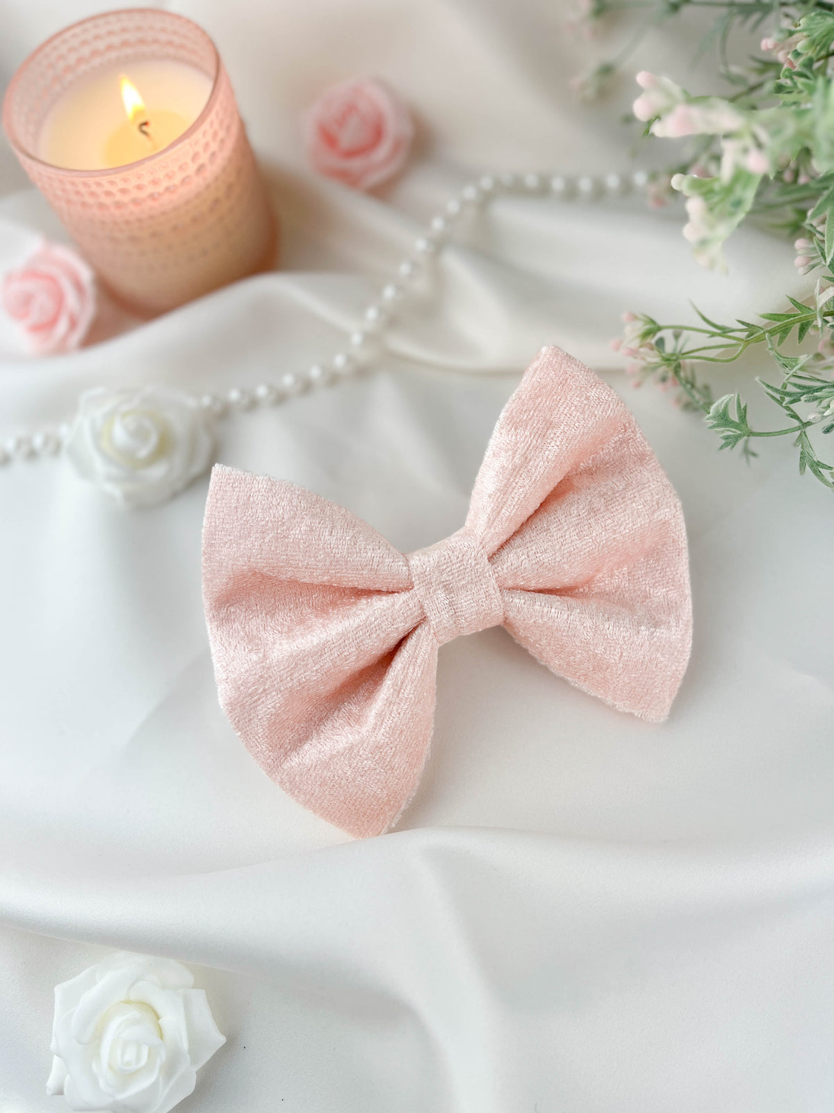 Pink bow with a candle, flowers, and pearls on a white surface