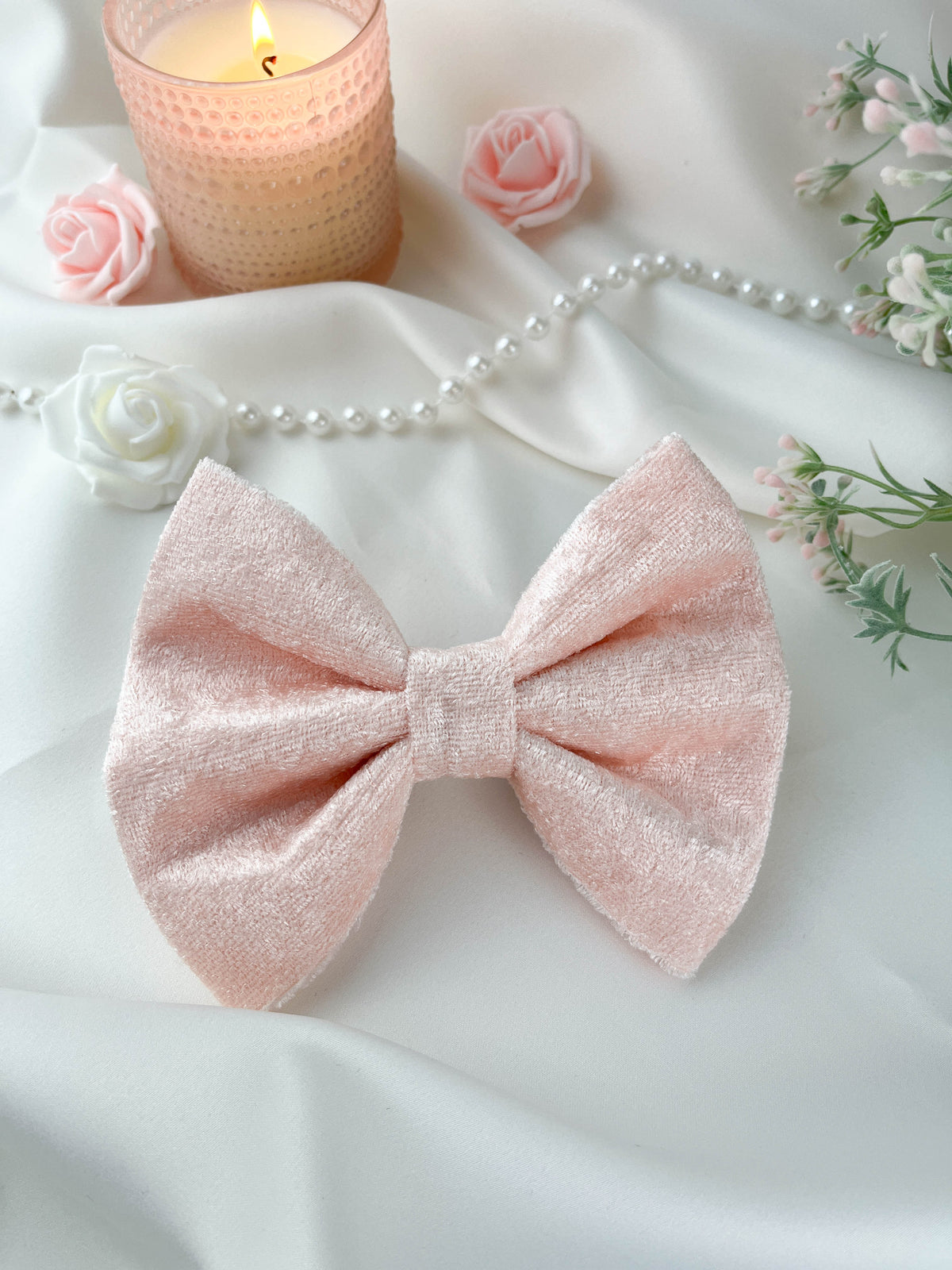 Pink bow with a candle, roses, and pearls on a white fabric background