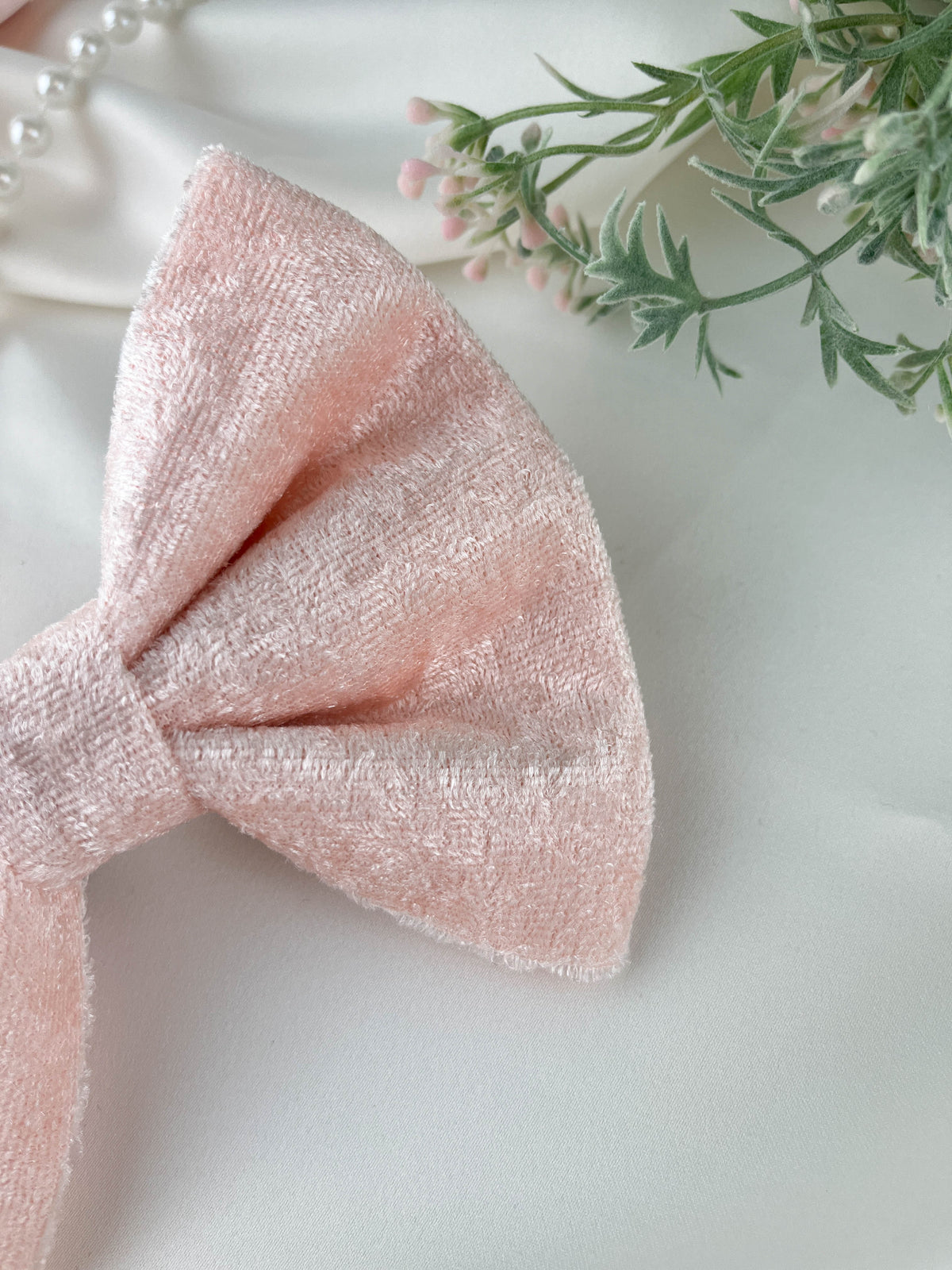 Pink bow on a white surface with greenery in the background
