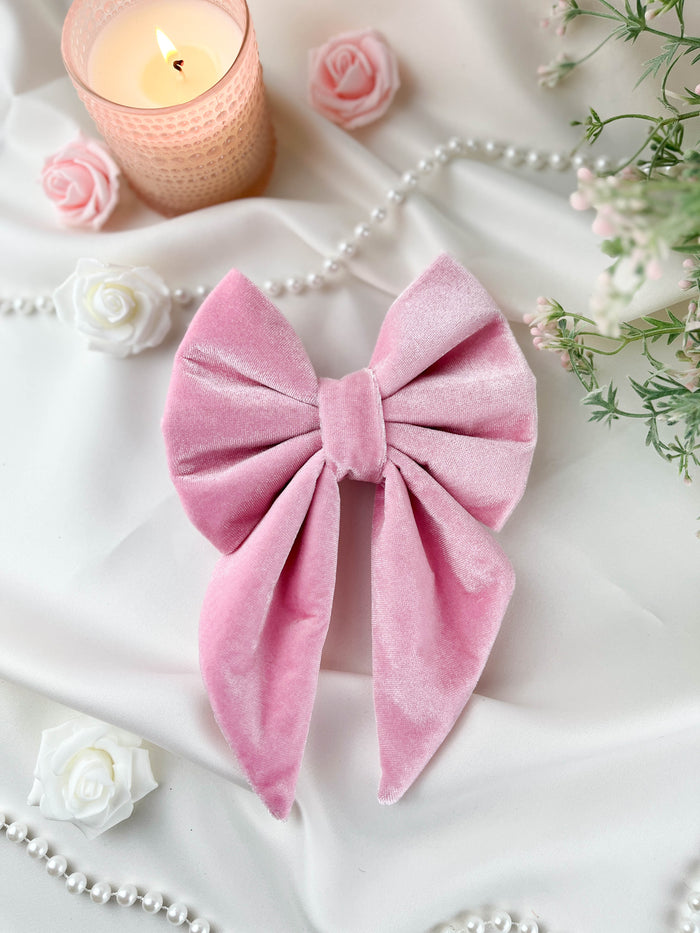 Pink velvet bow with candles, flowers, and pearls on a white fabric background