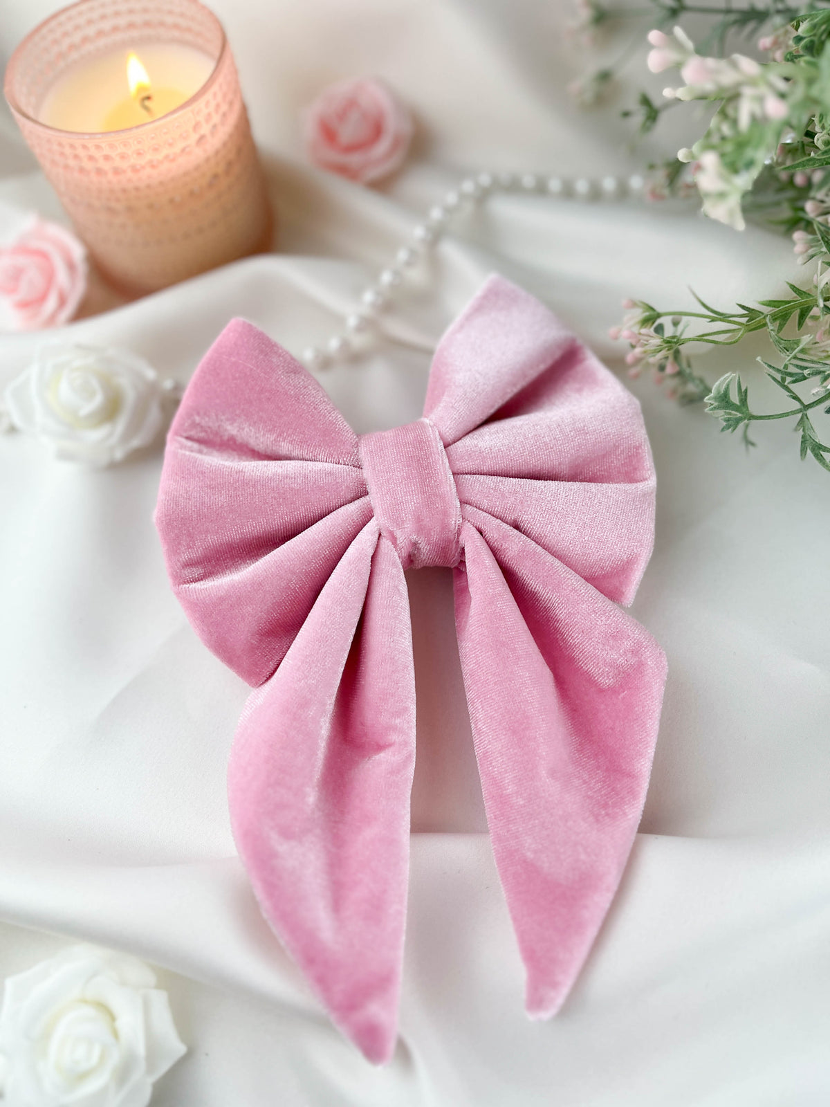 Pink velvet bow with a candle and flowers on a white surface