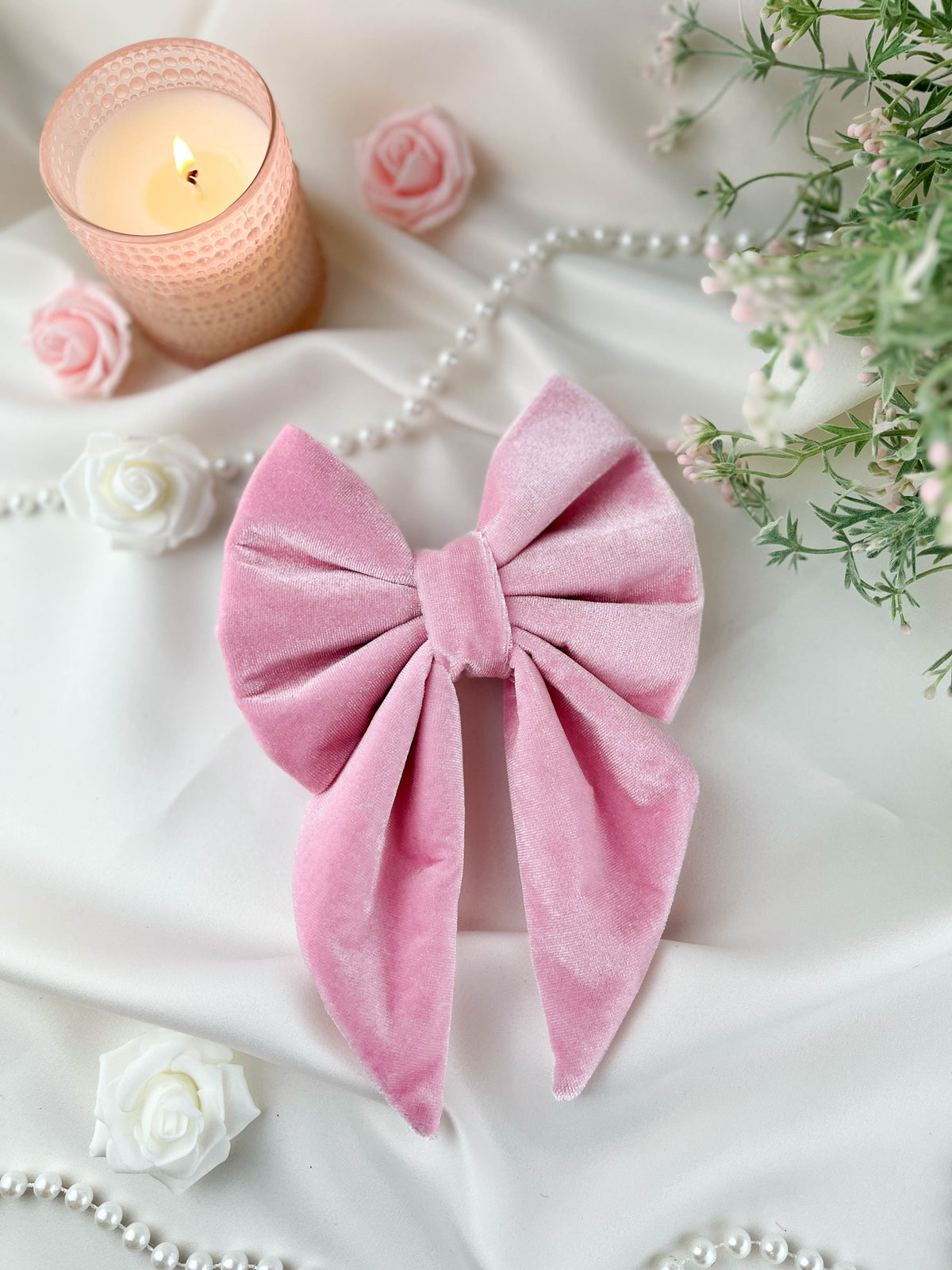 Pink velvet bow with a candle, pearls, and flowers on a white surface