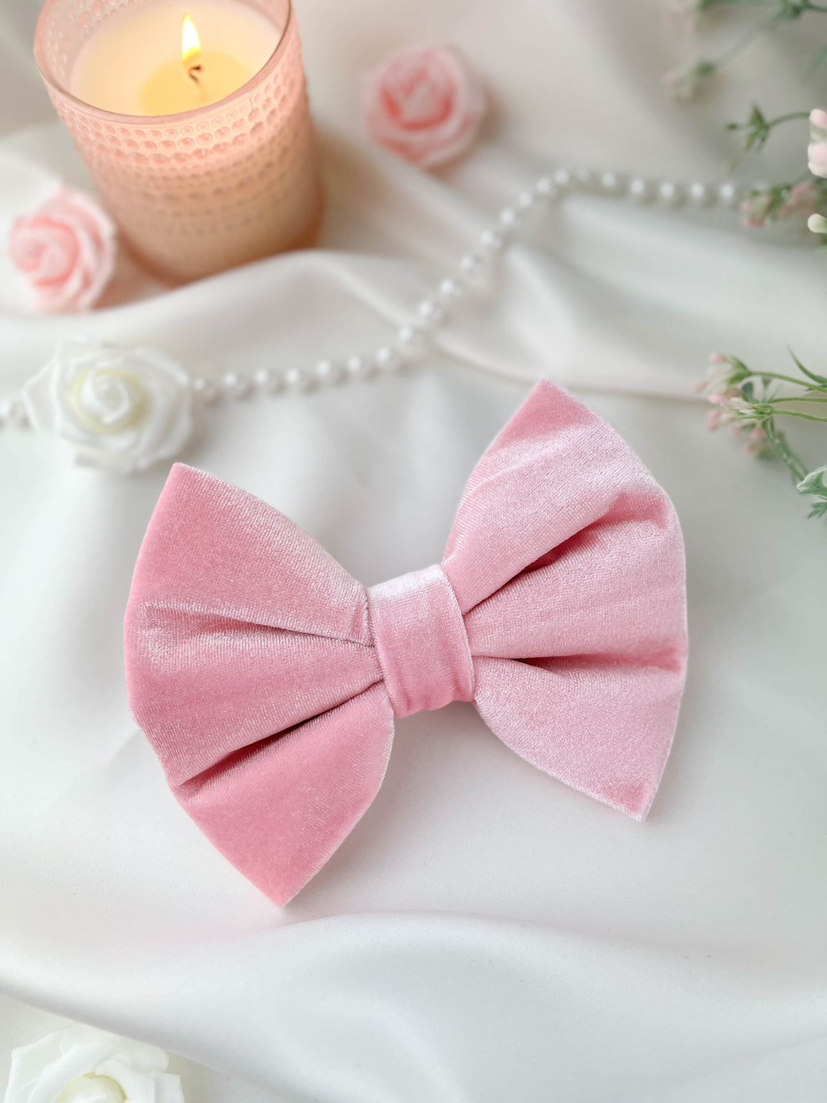 Pink velvet bow with a soft focus background featuring flowers and a candle.