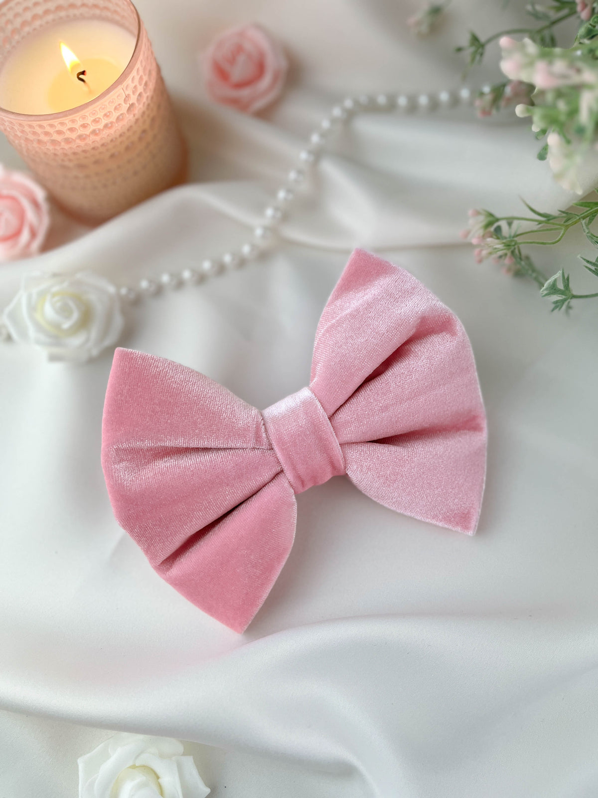 Pink velvet bow with a candle, pearls, and flowers on a white surface