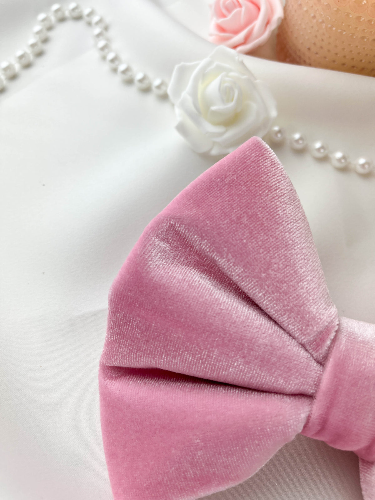 Pink velvet bow with white roses and pearls on a white background