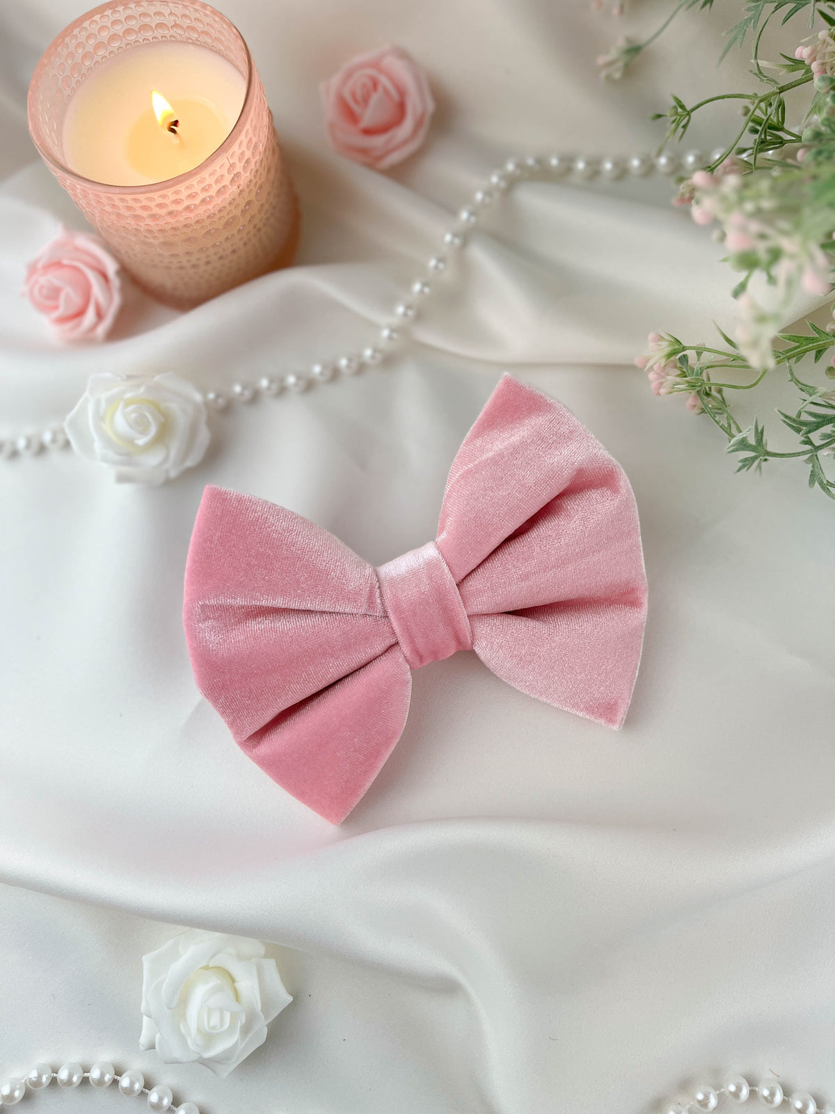 Pink velvet bow with candles, flowers, and pearls on a white surface
