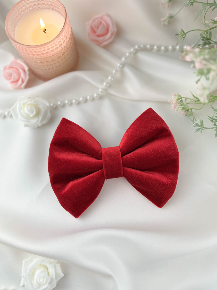 Red bow tie on a white surface with a lit candle and flowers in the background