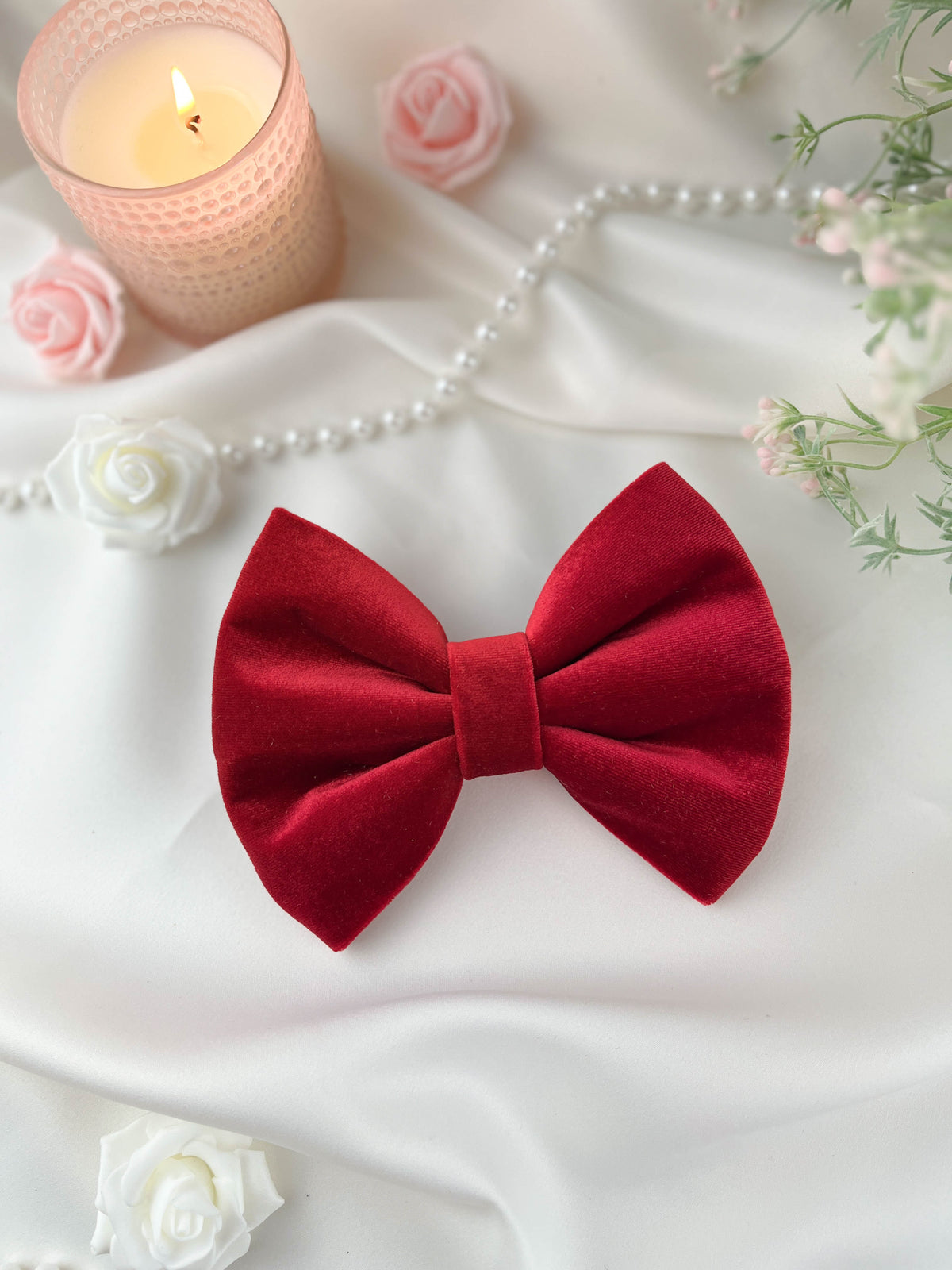 Red bow tie on a white fabric background with flowers and a candle.