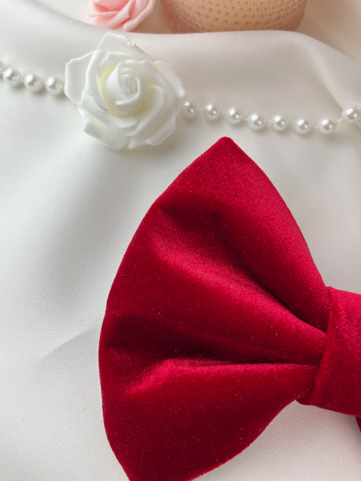 Red bow tie with a white rose and pearl necklace on a white background