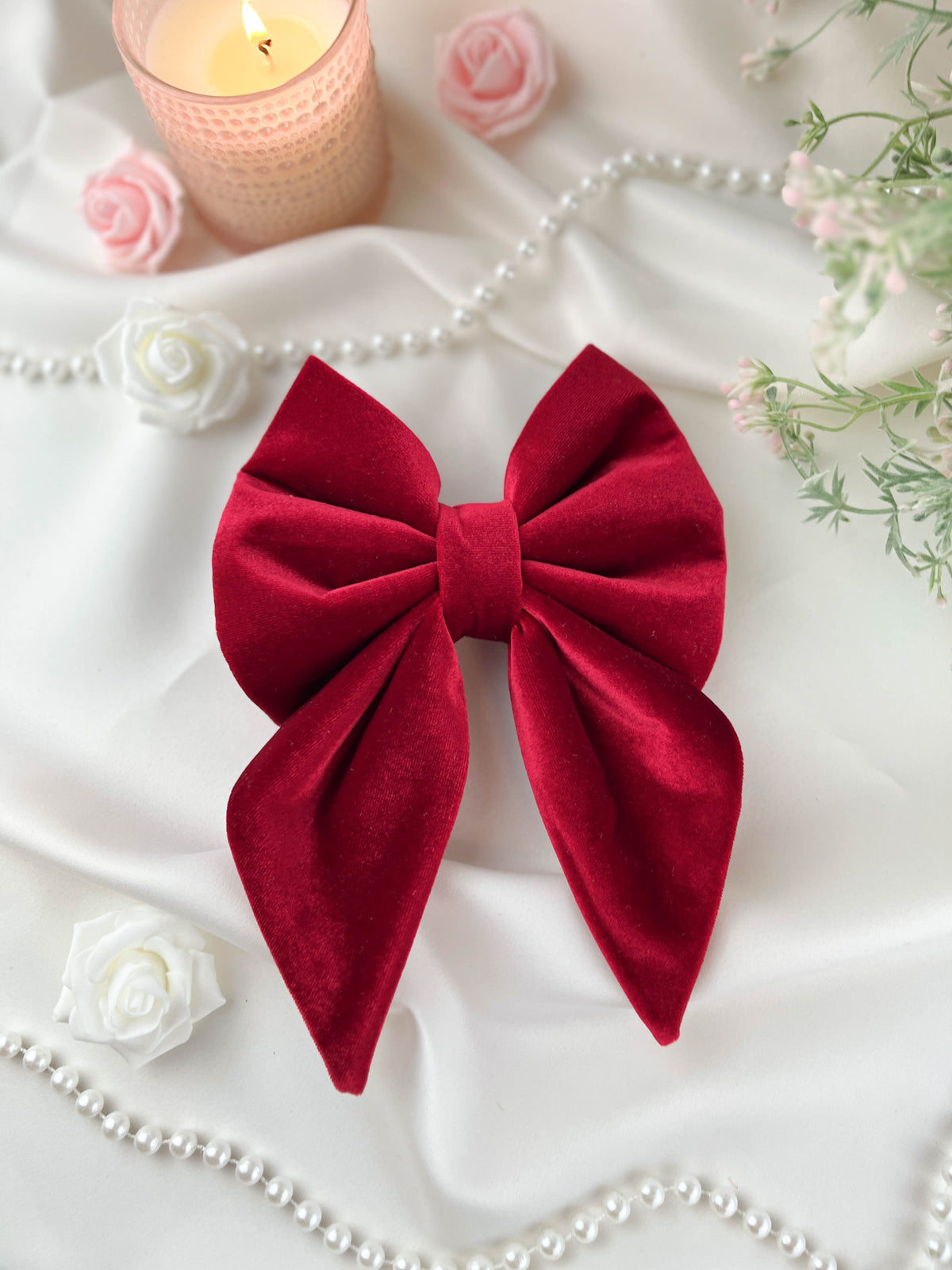 Red bow with a candle, flowers, and pearls on a white background