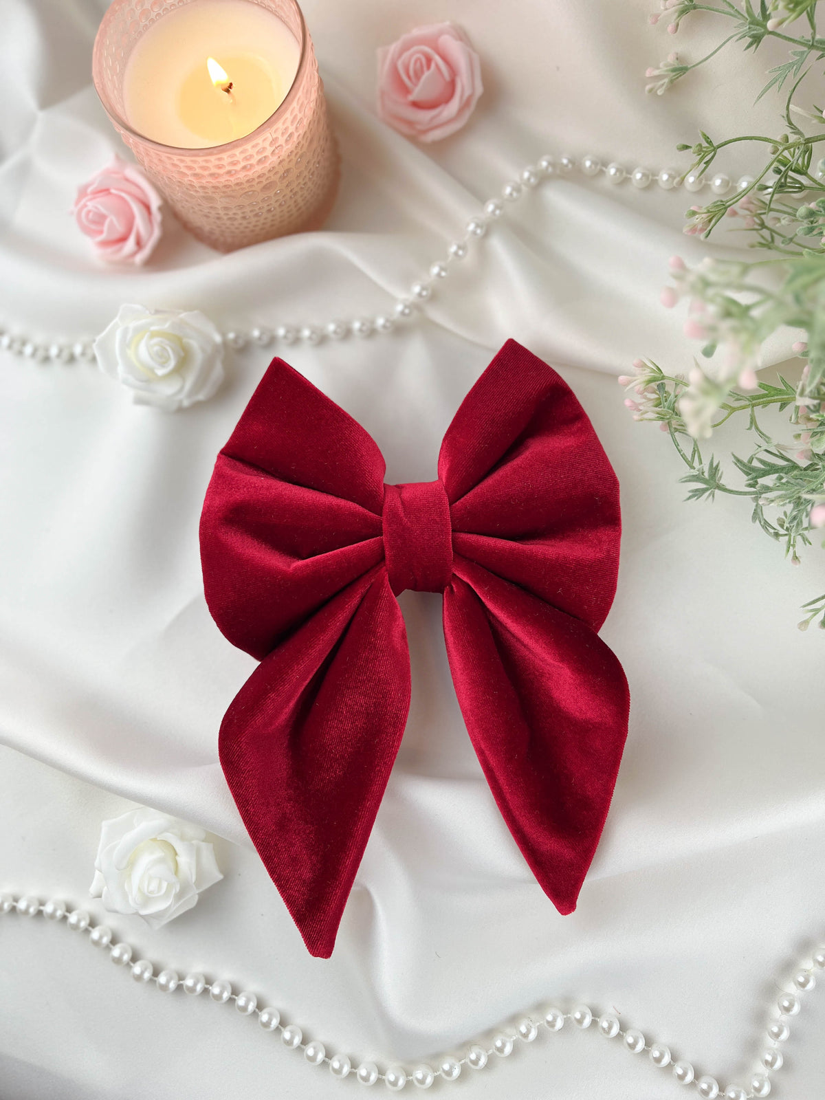 Red bow on a white fabric background with flowers and a candle.