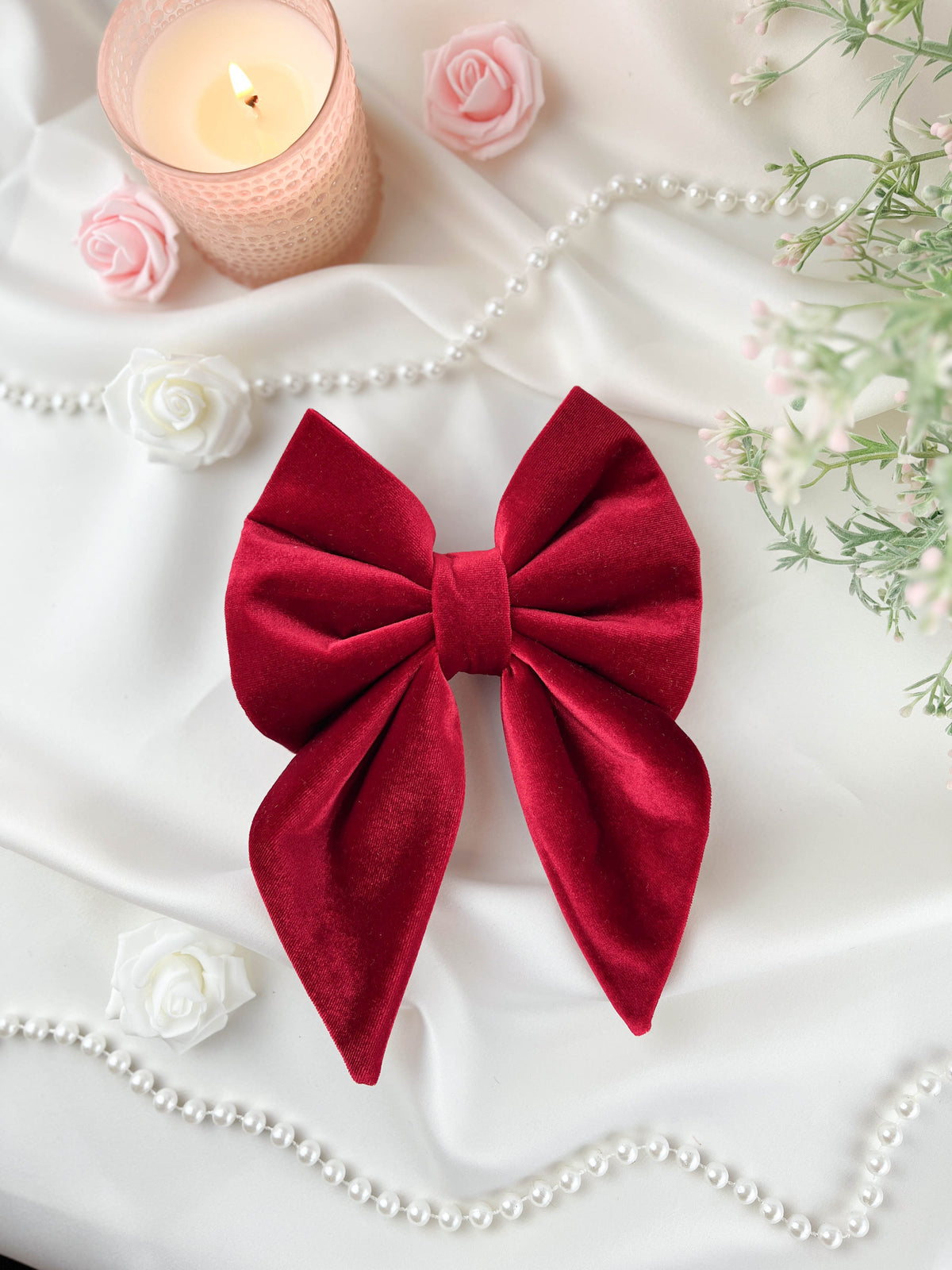 Red bow with a candle, flowers, and pearls on a white surface