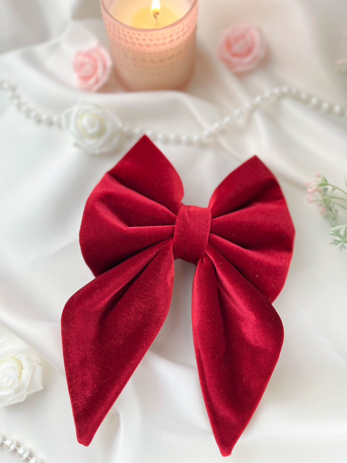 Red bow with a candle and flowers on a white surface