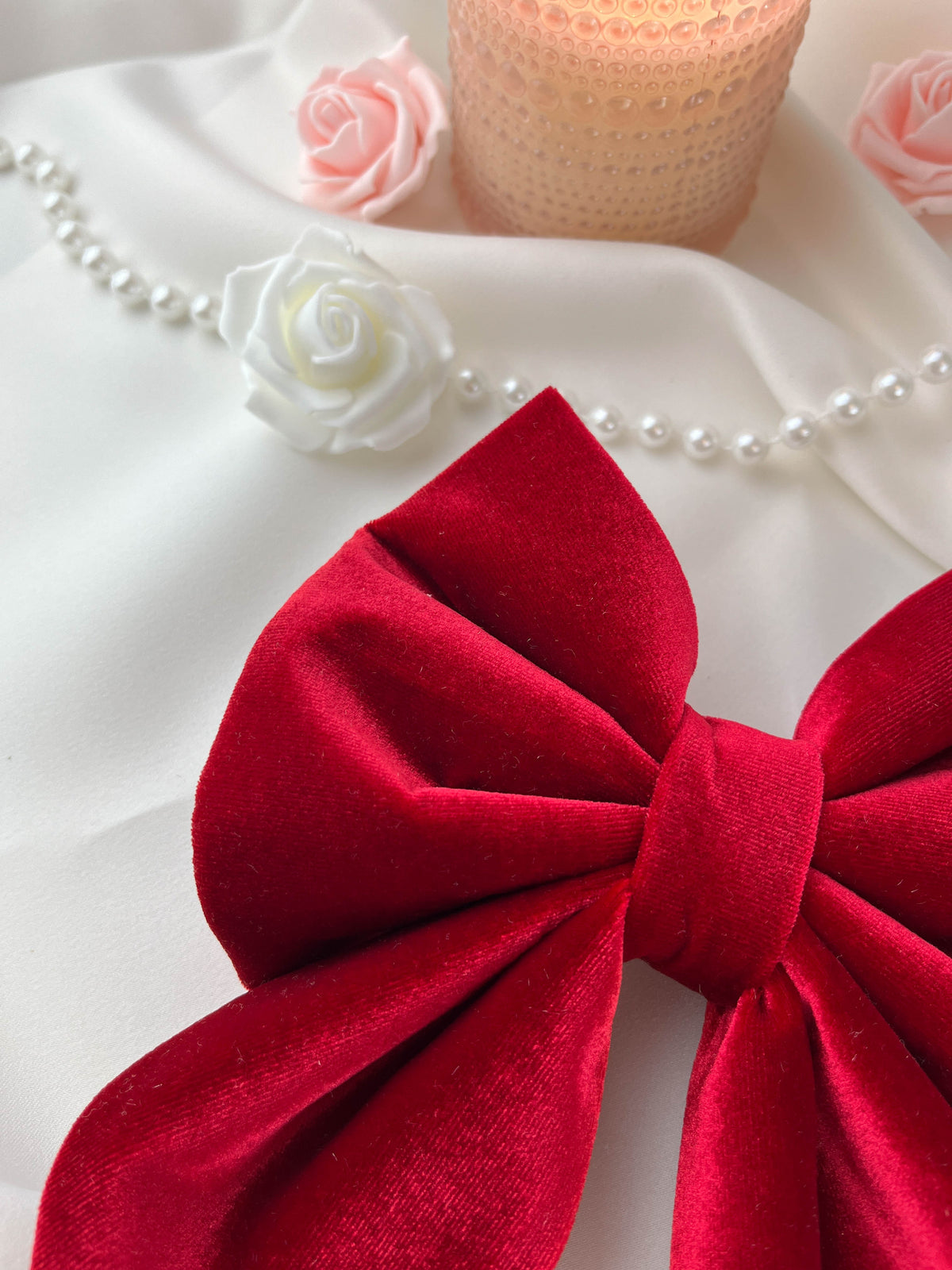 Red bow with white and pink roses and a pearl necklace on a white background
