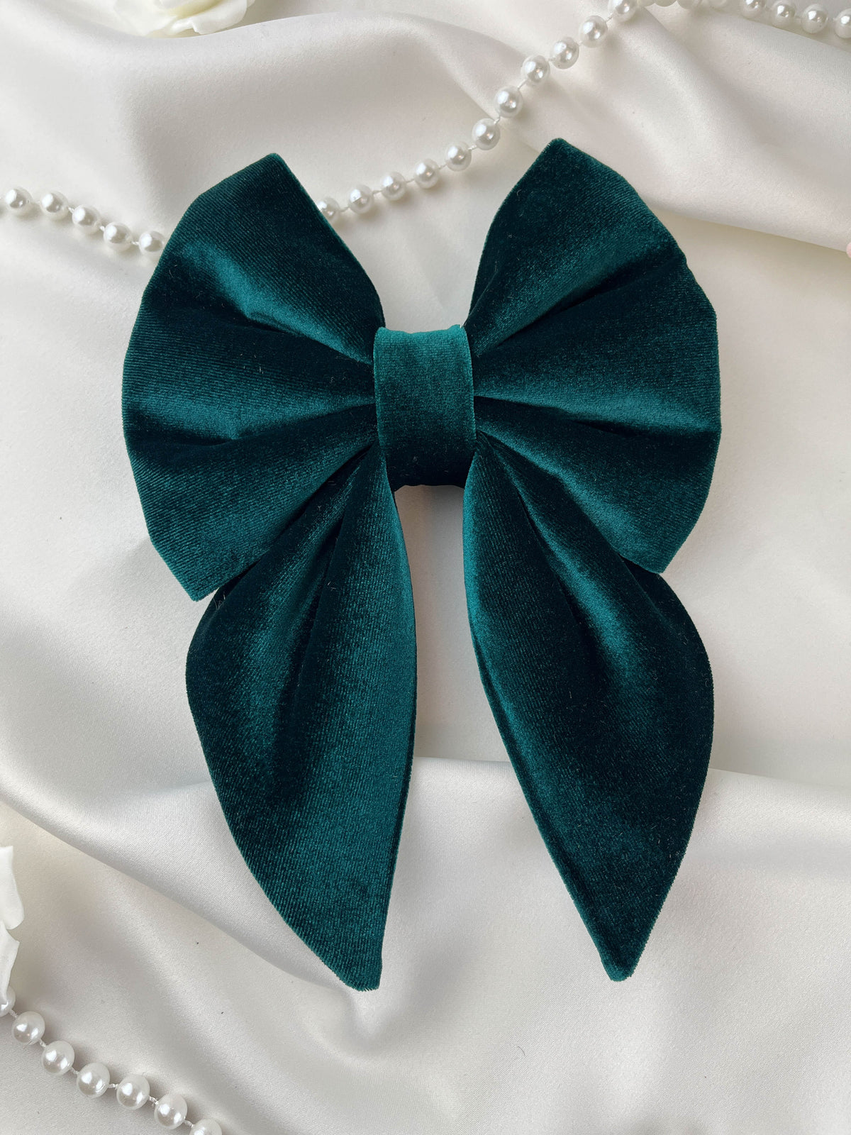 Green bow with pearl necklace on white fabric background