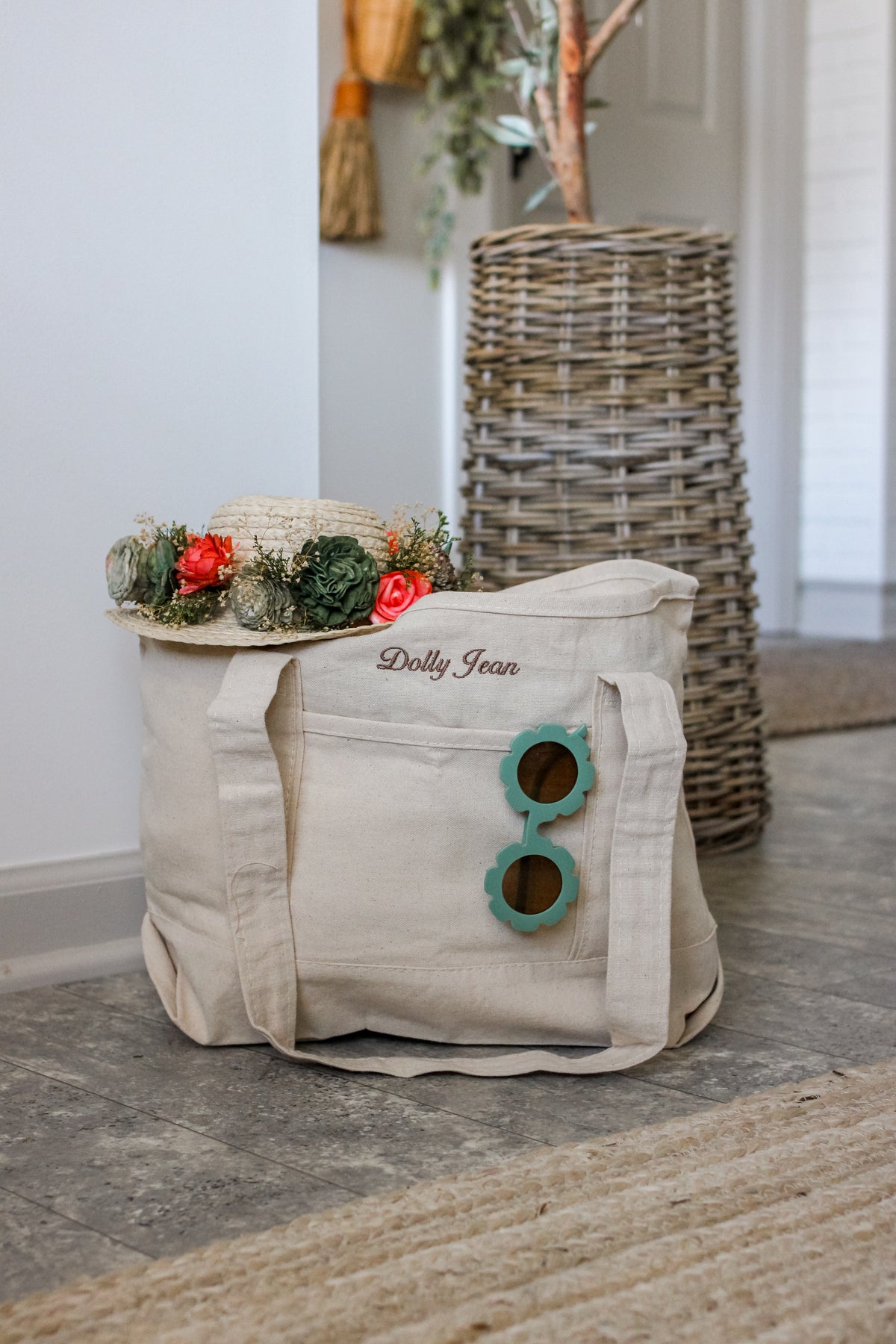 Beige embroidered tote bag with floral arrangement and sunglasses on a wooden floor