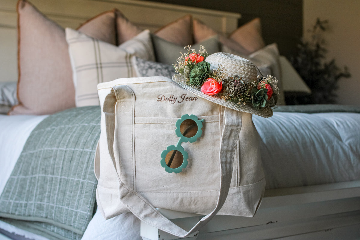 Beige embroidered tote bag with floral design on a bed with pillows