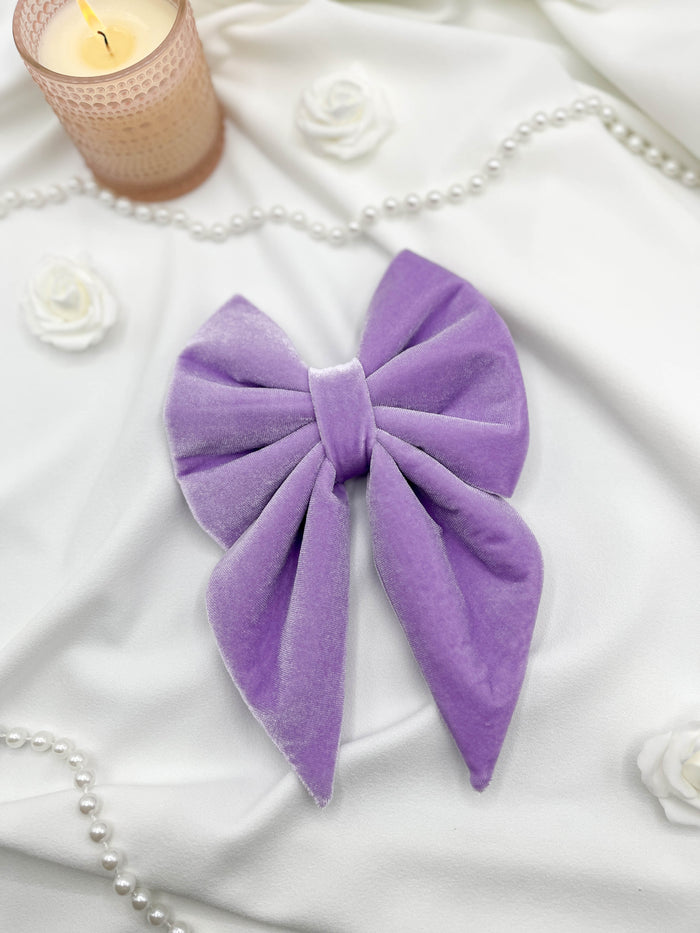 Purple bow on a white fabric background with candles and pearls.