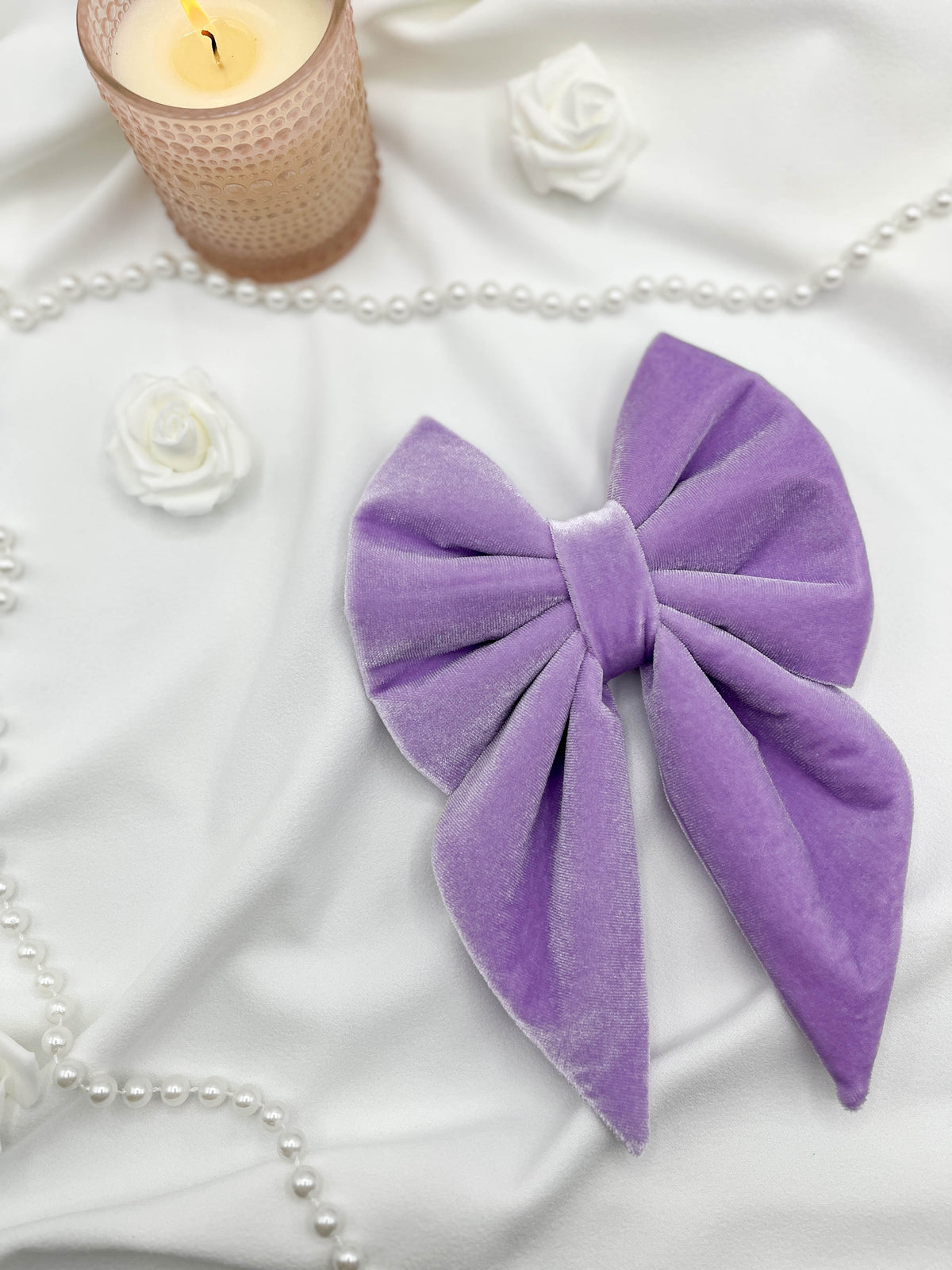 Purple bow on a white surface with a candle and flowers in the background