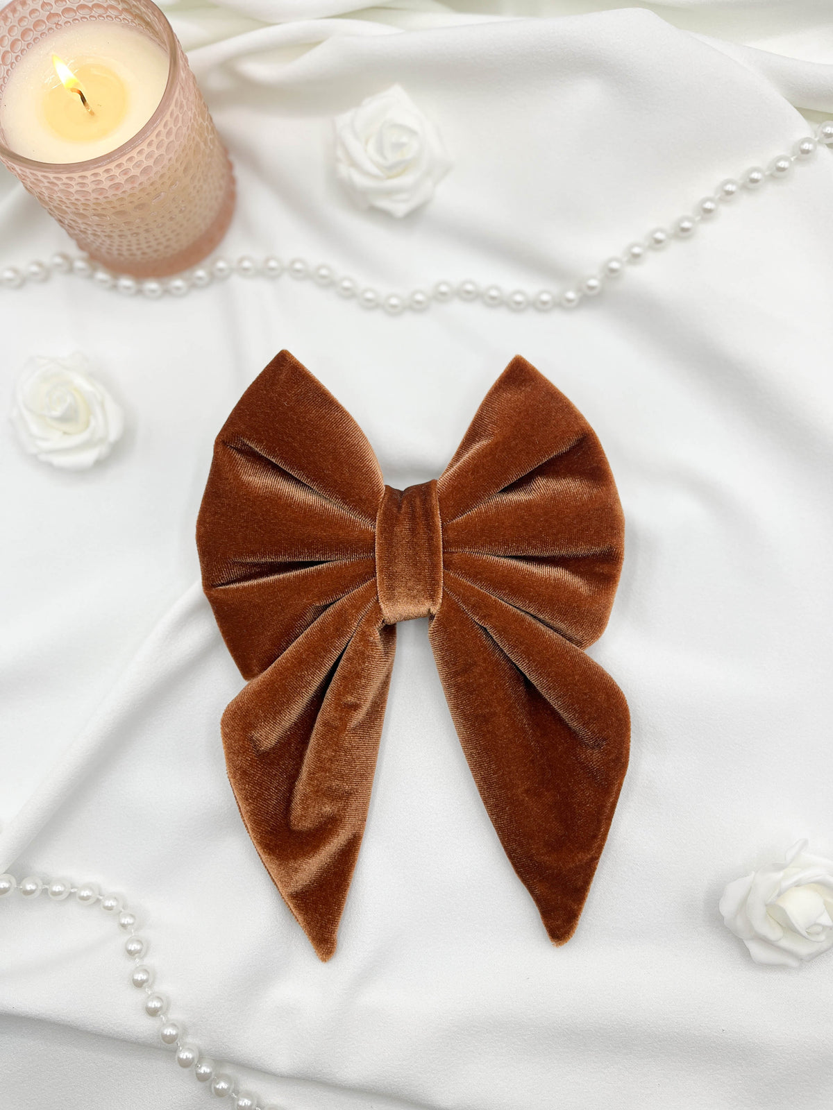 Brown velvet bow with a candle and pearls on a white surface