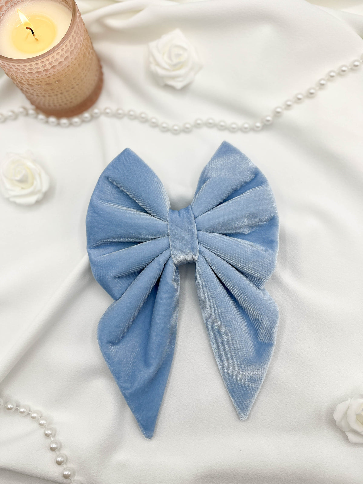 Blue bow on a white surface with a candle and pearls in the background