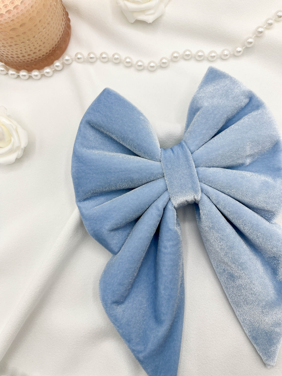 Blue velvet bow on a white background with pearls and flowers.