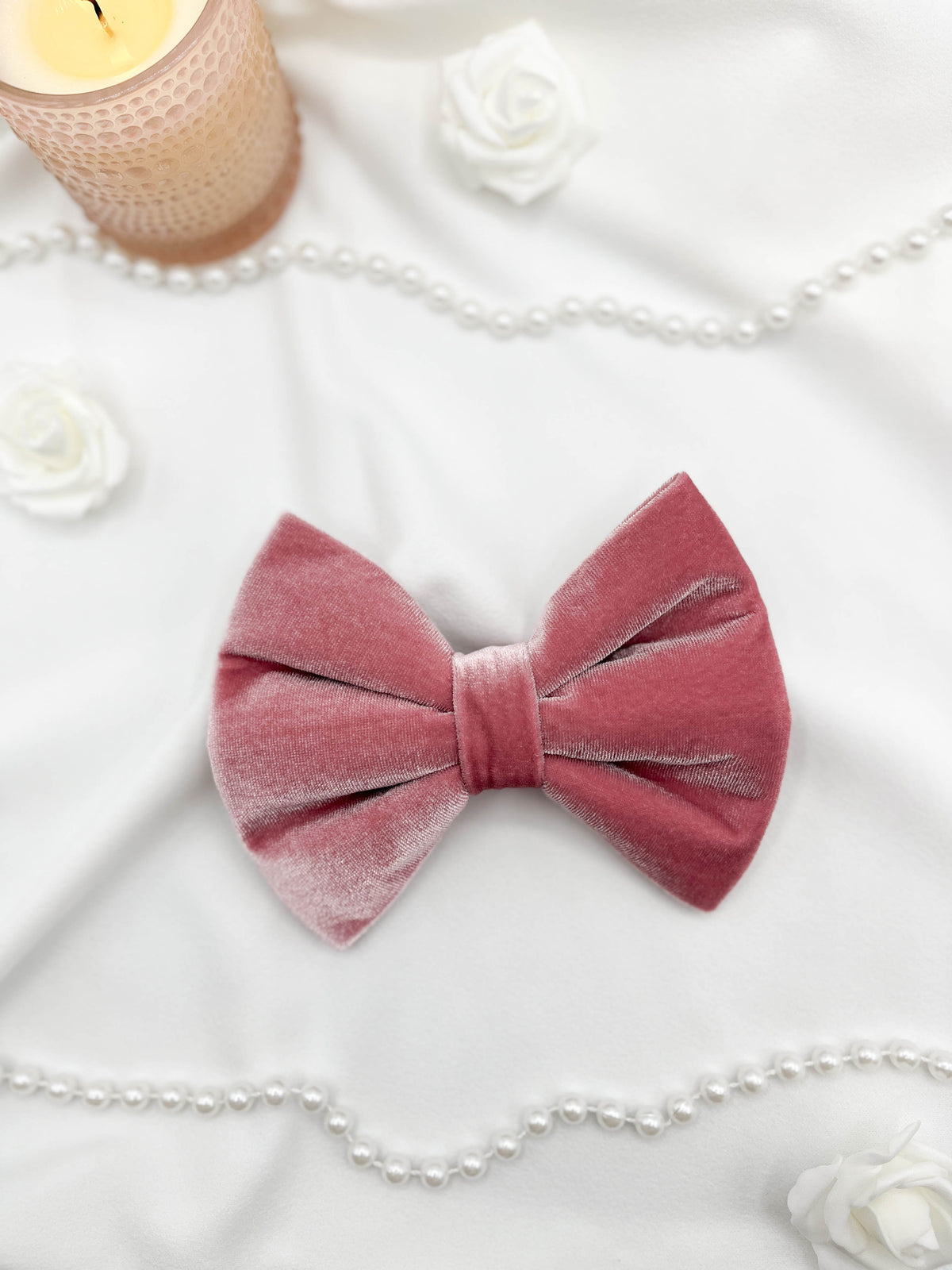 Pink velvet bow with white flowers and a candle on a white background