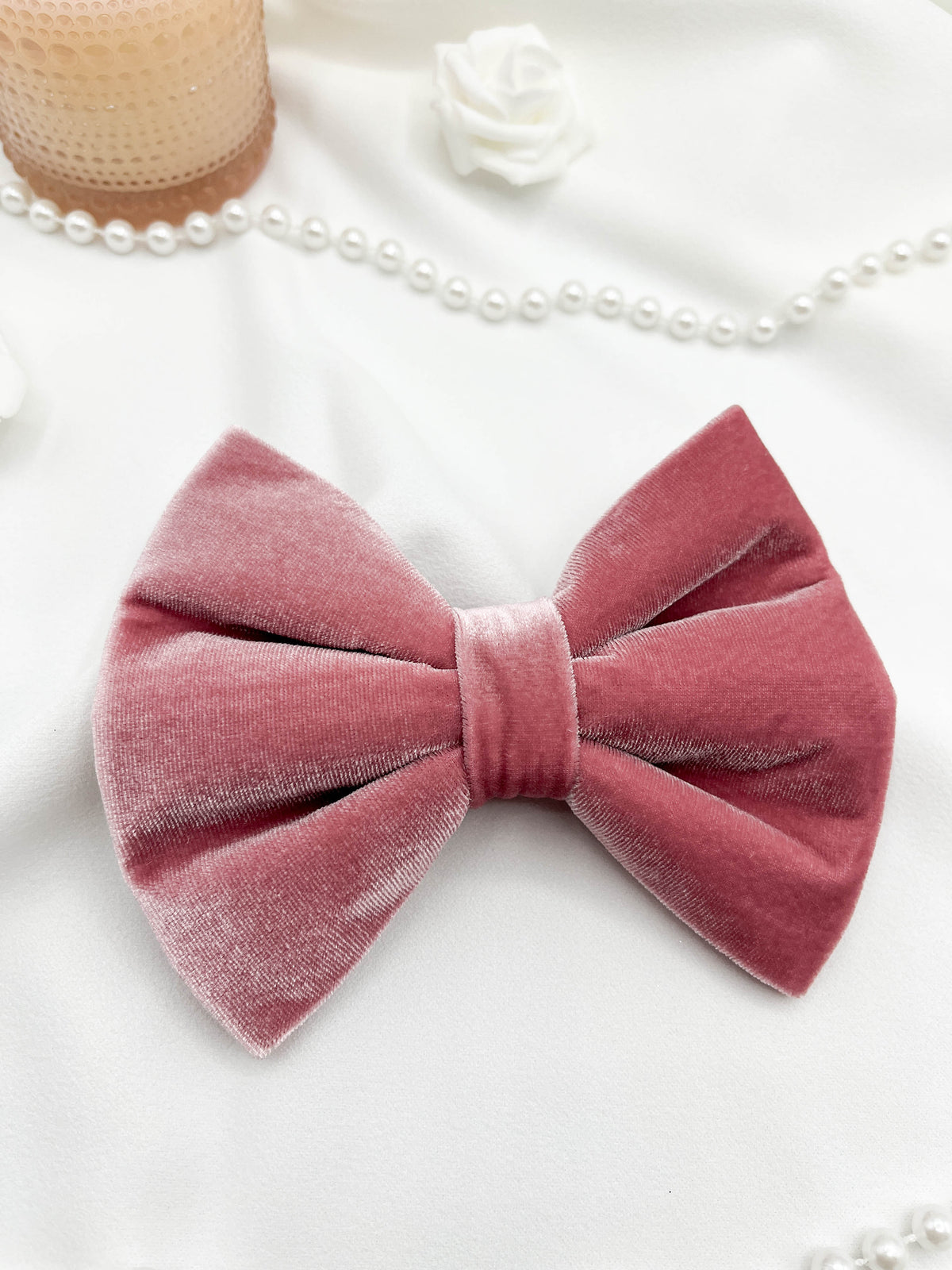 Pink velvet bow on a white background with pearls and a candle.