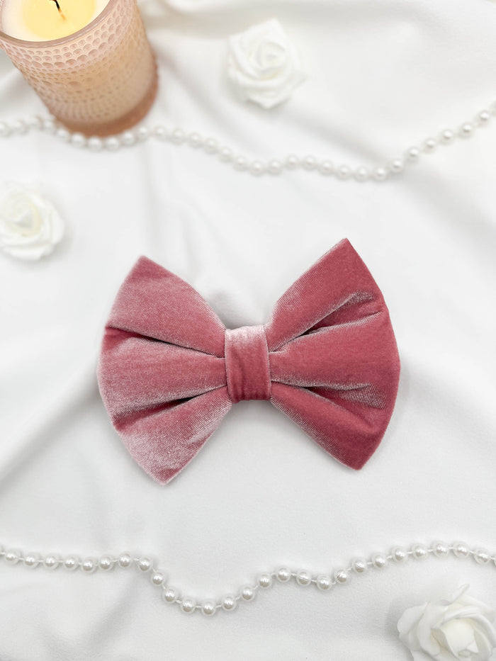 Pink velvet bow with a candle, pearls, and flowers on a white surface