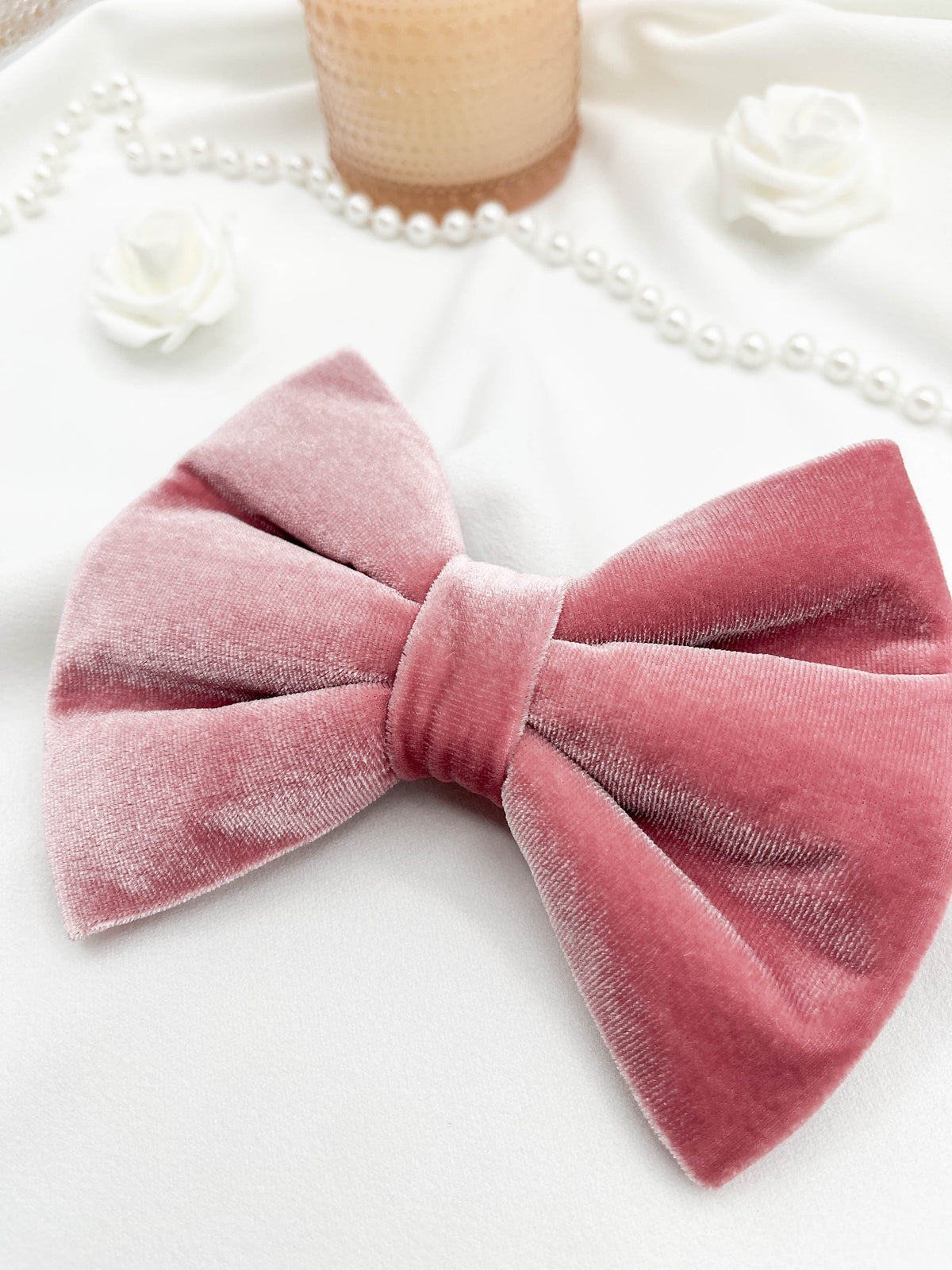 Pink velvet bow with pearls and a candle in the background