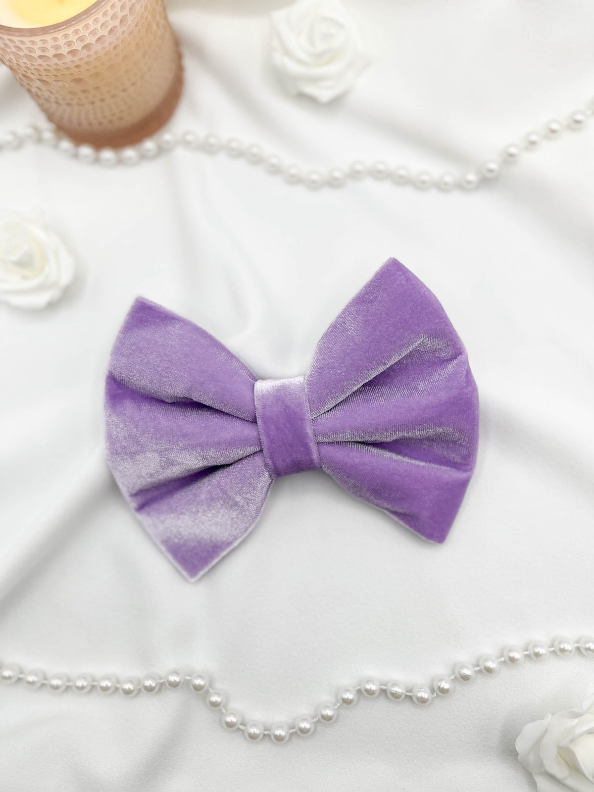 Purple bow tie on a white surface with pearls and flowers