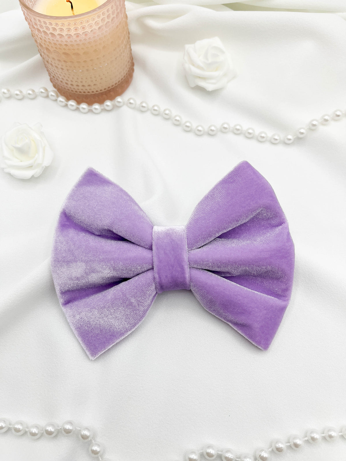 Purple velvet bow with pearls and a candle on a white surface