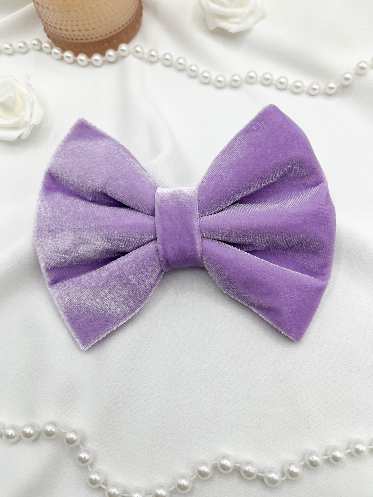 Purple velvet bow with pearl necklace and flowers on a white background