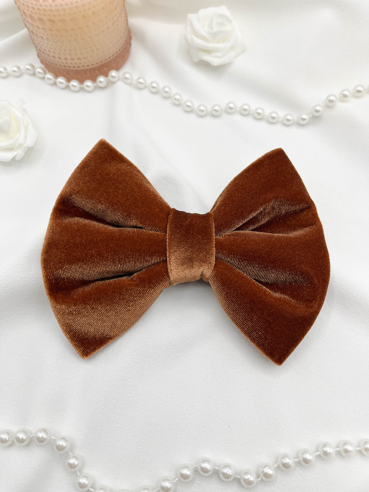 Brown velvet bow on a white surface with pearls and flowers
