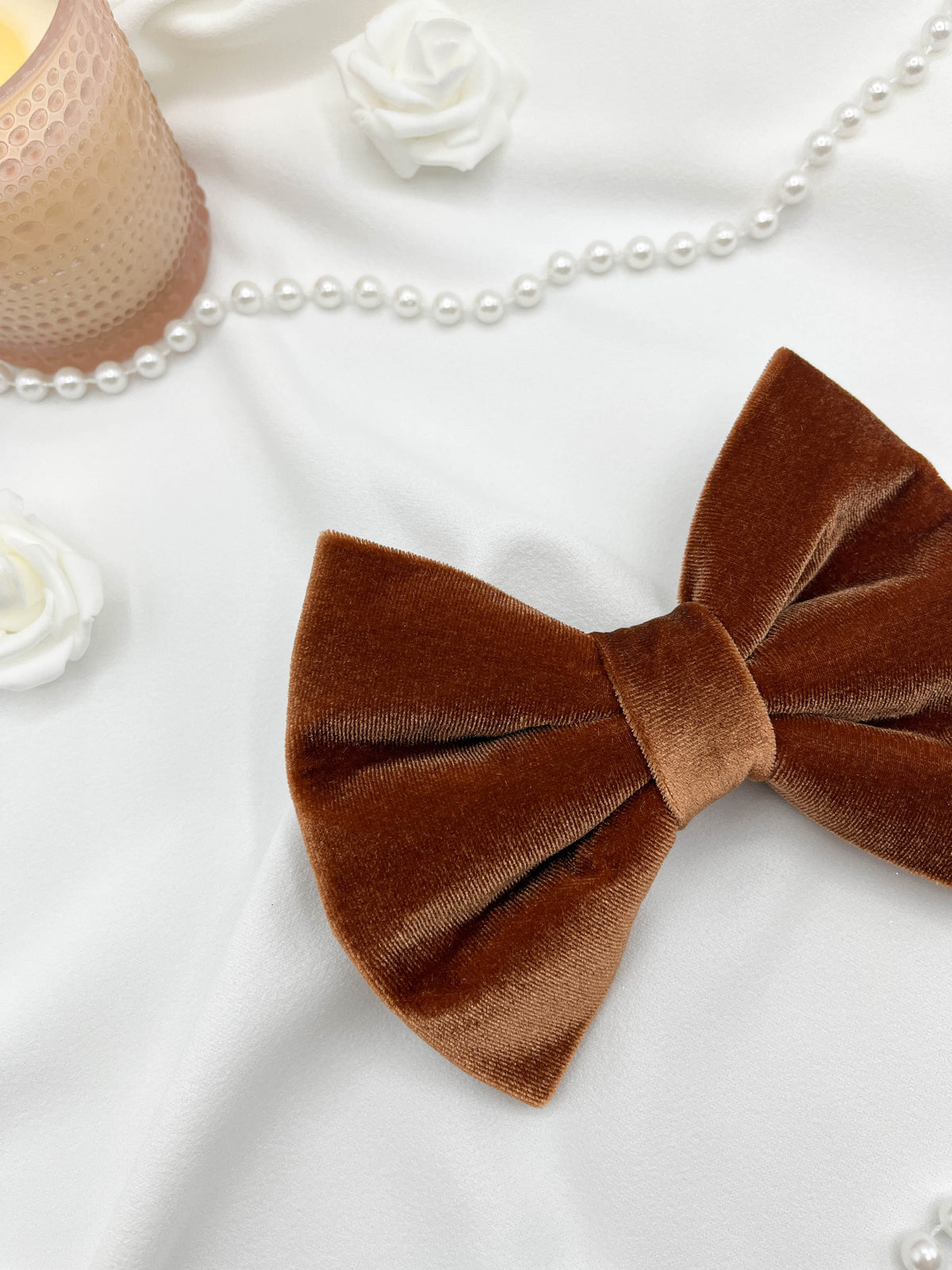 Brown velvet bow on a white surface with pearls and flowers in the background
