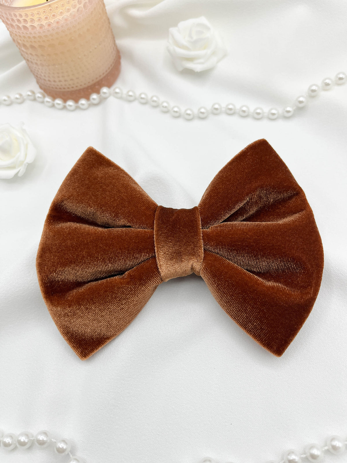 Brown velvet bow with candles and pearls on a white surface