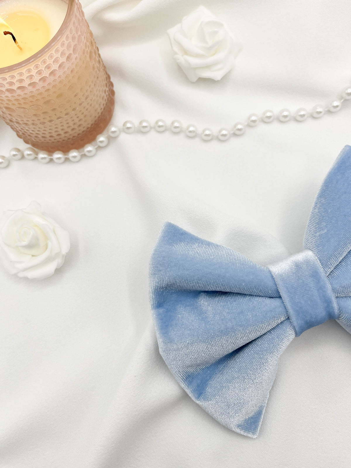 Blue bow tie on a white surface with pearls and candles in the background