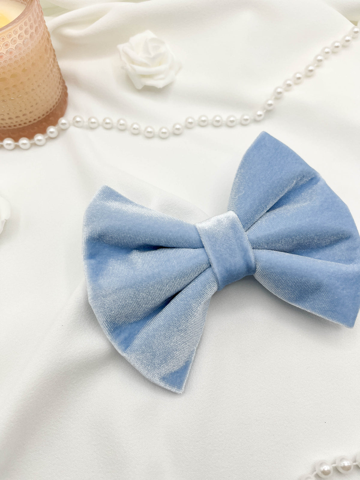 Light blue bow tie on a white background with pearls and a candle.
