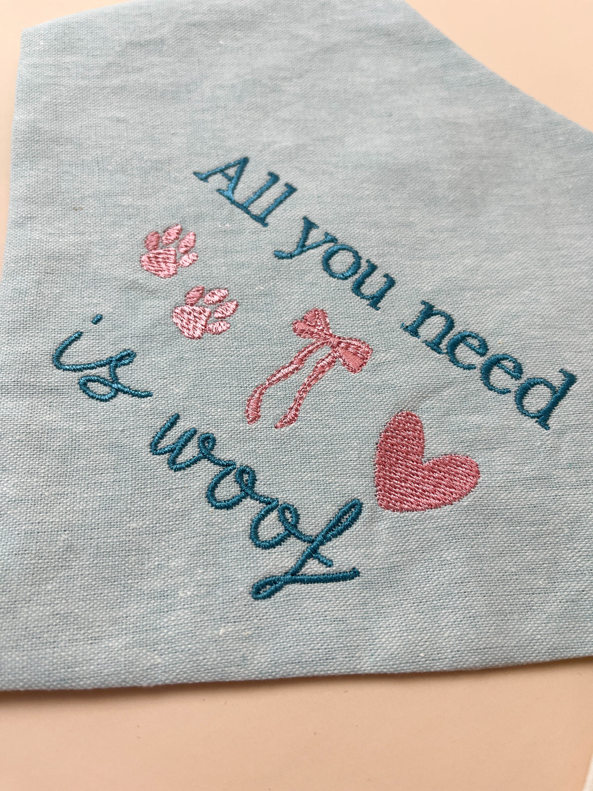Embroidered text on a light blue dog bandana with hearts and bows