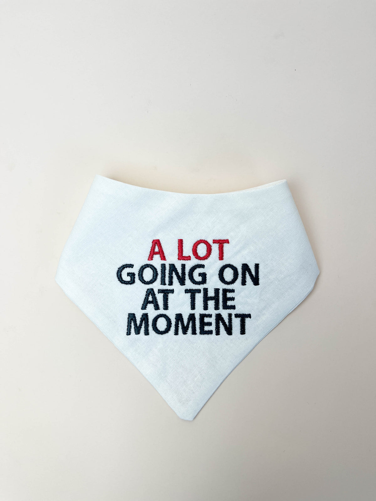 White bandana with text 'A LOT GOING ON AT THE MOMENT' on a beige background