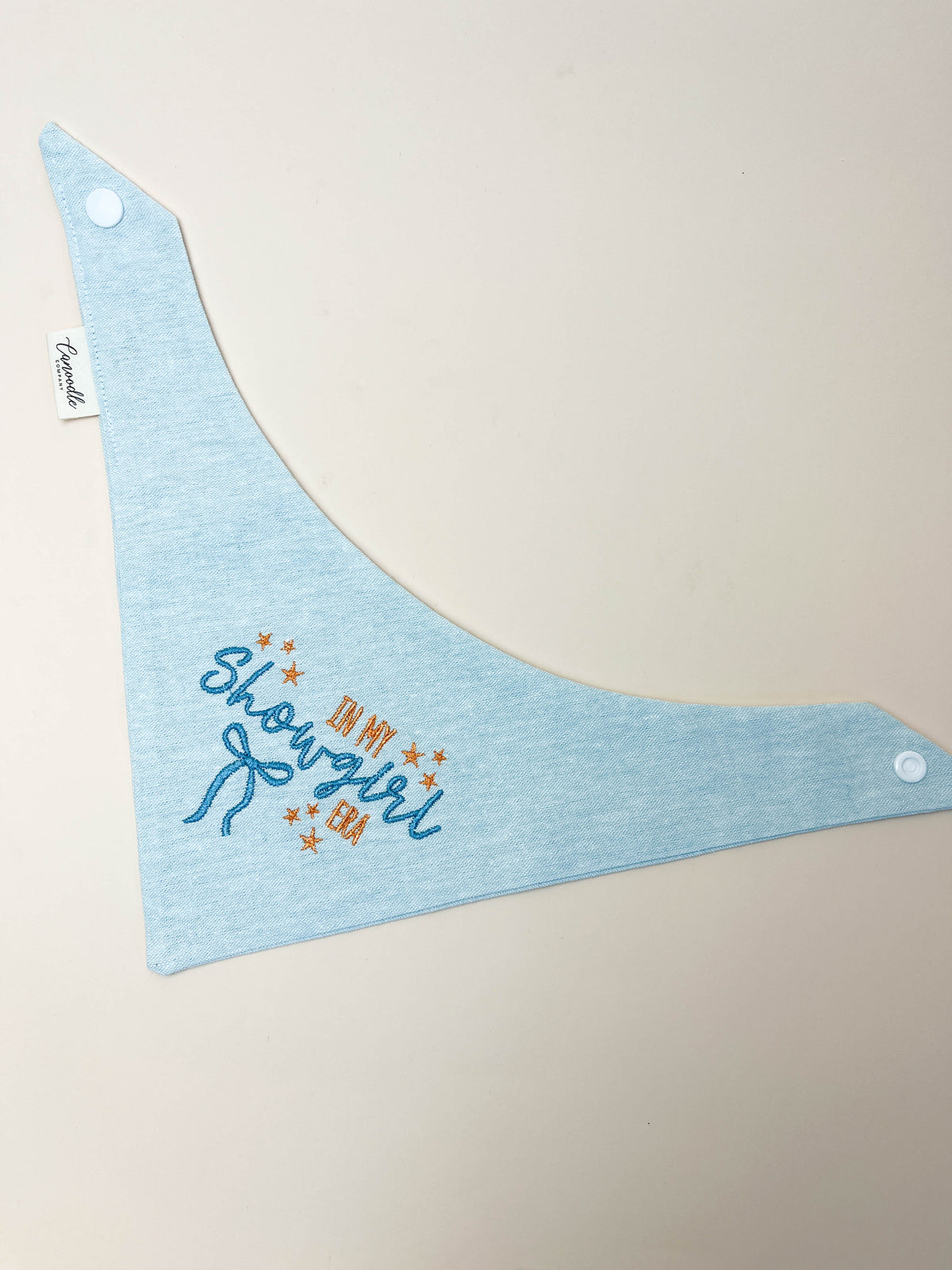 Light blue dog bib with 'Showgirl' text on a beige background