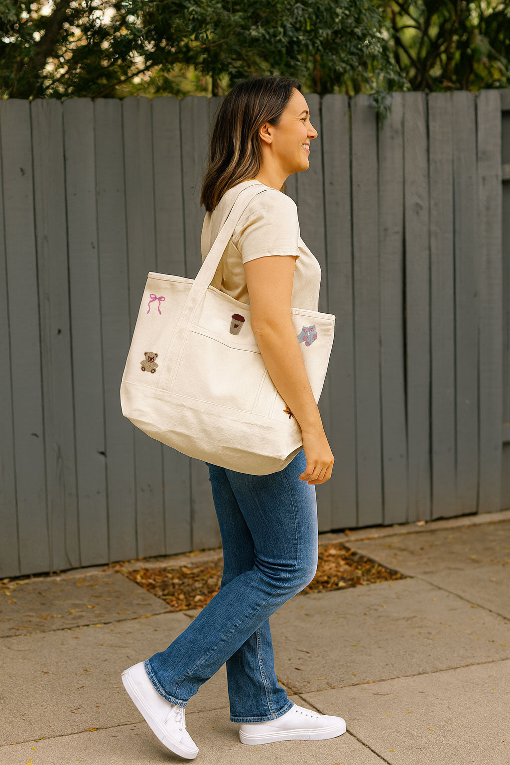 Woman walking outdoors with a white tote bag that has many embroidered icons on it