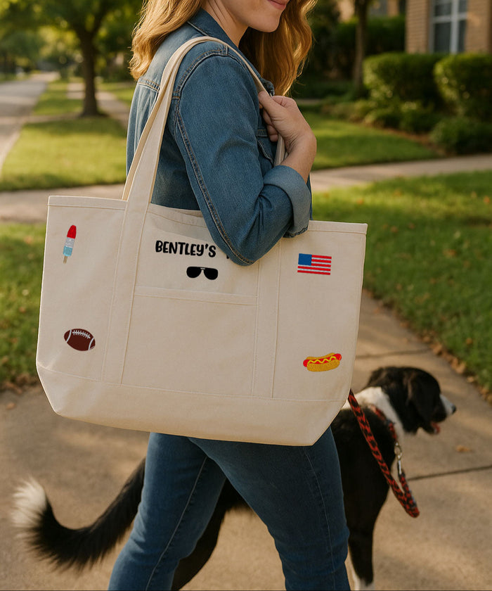 Person holding a tote bag with various embroidery graphics or icons, walking a dog on a suburban street.