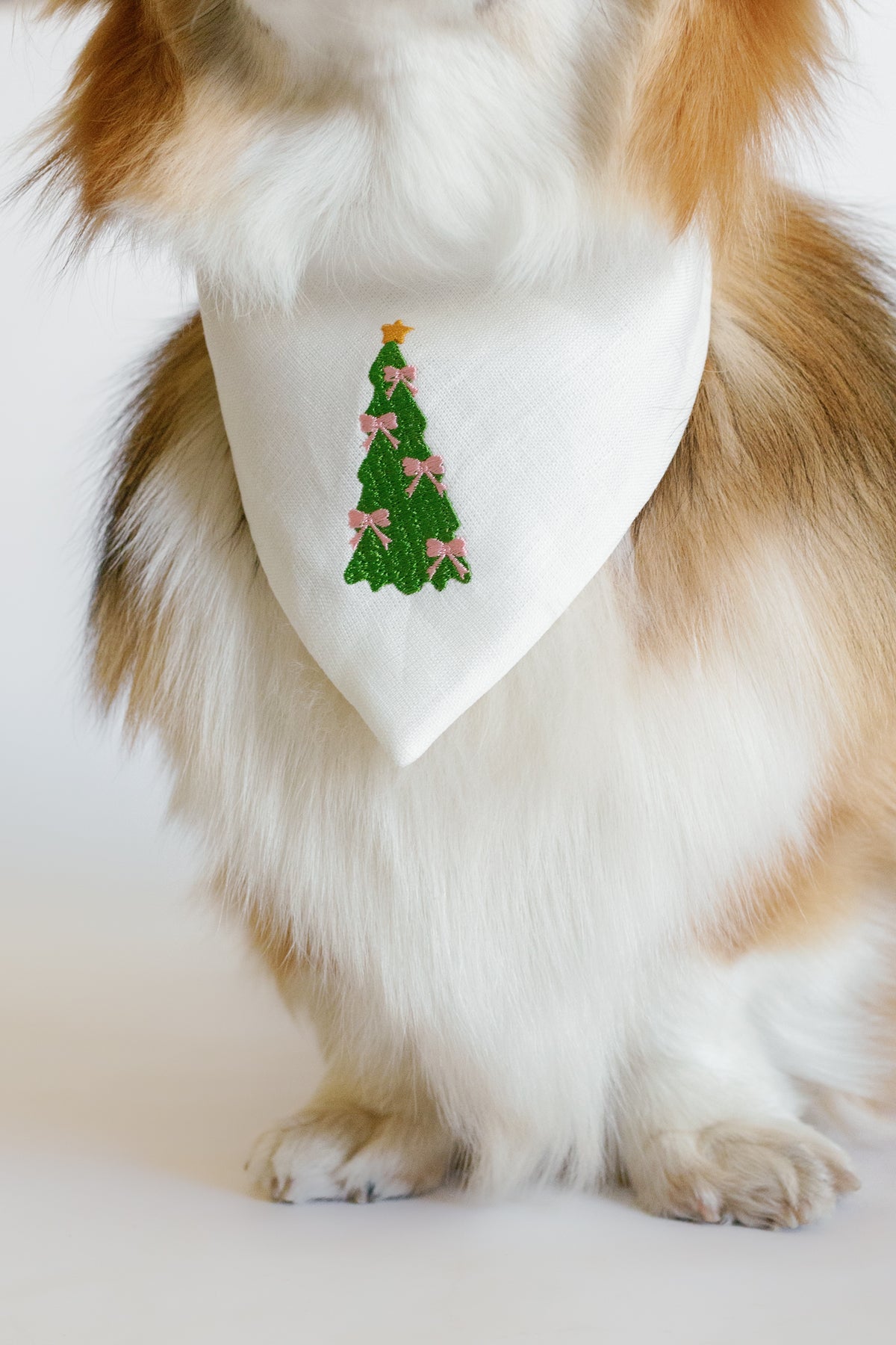 Dog wearing a white bandana with a Christmas tree design on a white background